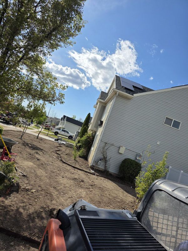 Backyard with a white house, dirt path, trees, and a metal fire pit in the foreground
