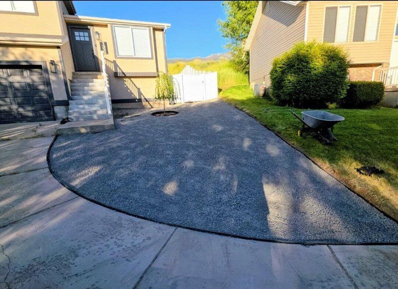 Curved concrete driveway beside a beige house, with stairs, lawn, and white gate in the background.