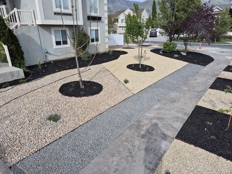 Landscaped apartment walkway with gravel, stepping stones, and young trees in mulch beds