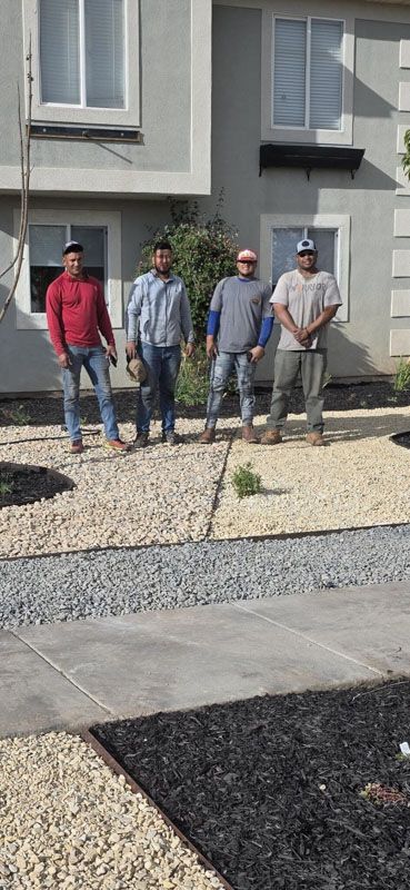 Four people stand outside a modern house in a landscaped front yard.