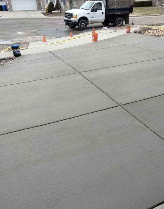 Fresh concrete sidewalk beside a street, with cones and a white utility truck in the background.
