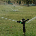 Sprinkler watering a grassy field with trees in the background