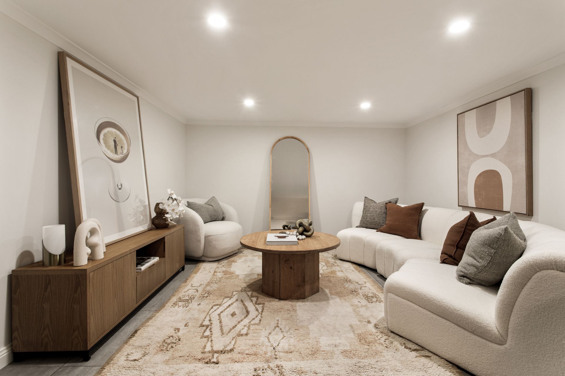 Modern neutral living room with white sofas, wood console, round coffee table, and abstract wall art