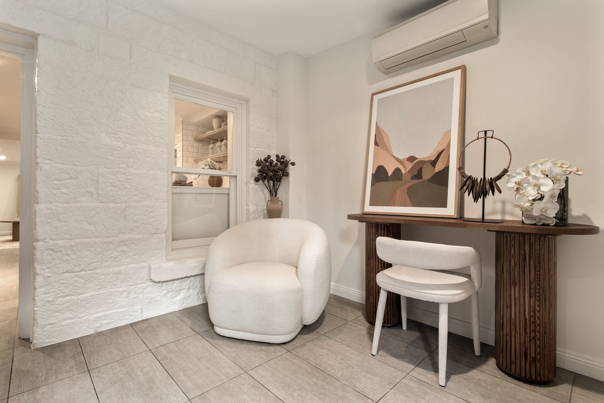 Cozy white seating nook with armchair, console table, mirror, and wall art in a bright tiled room
