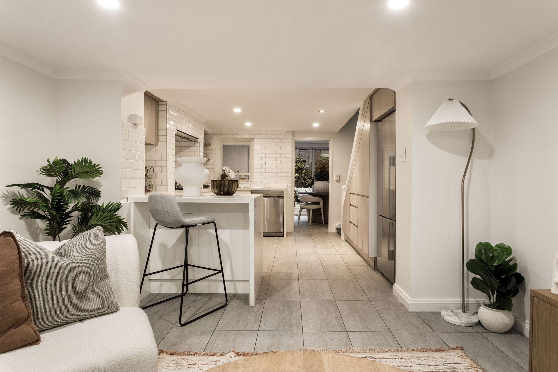 Bright, modern open-plan living room and kitchen with white walls, bar stools, and indoor plants.