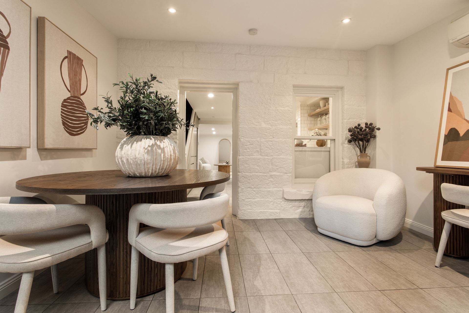 Cozy beige living room with round table, white chairs, armchair, wall art, and wood floor
