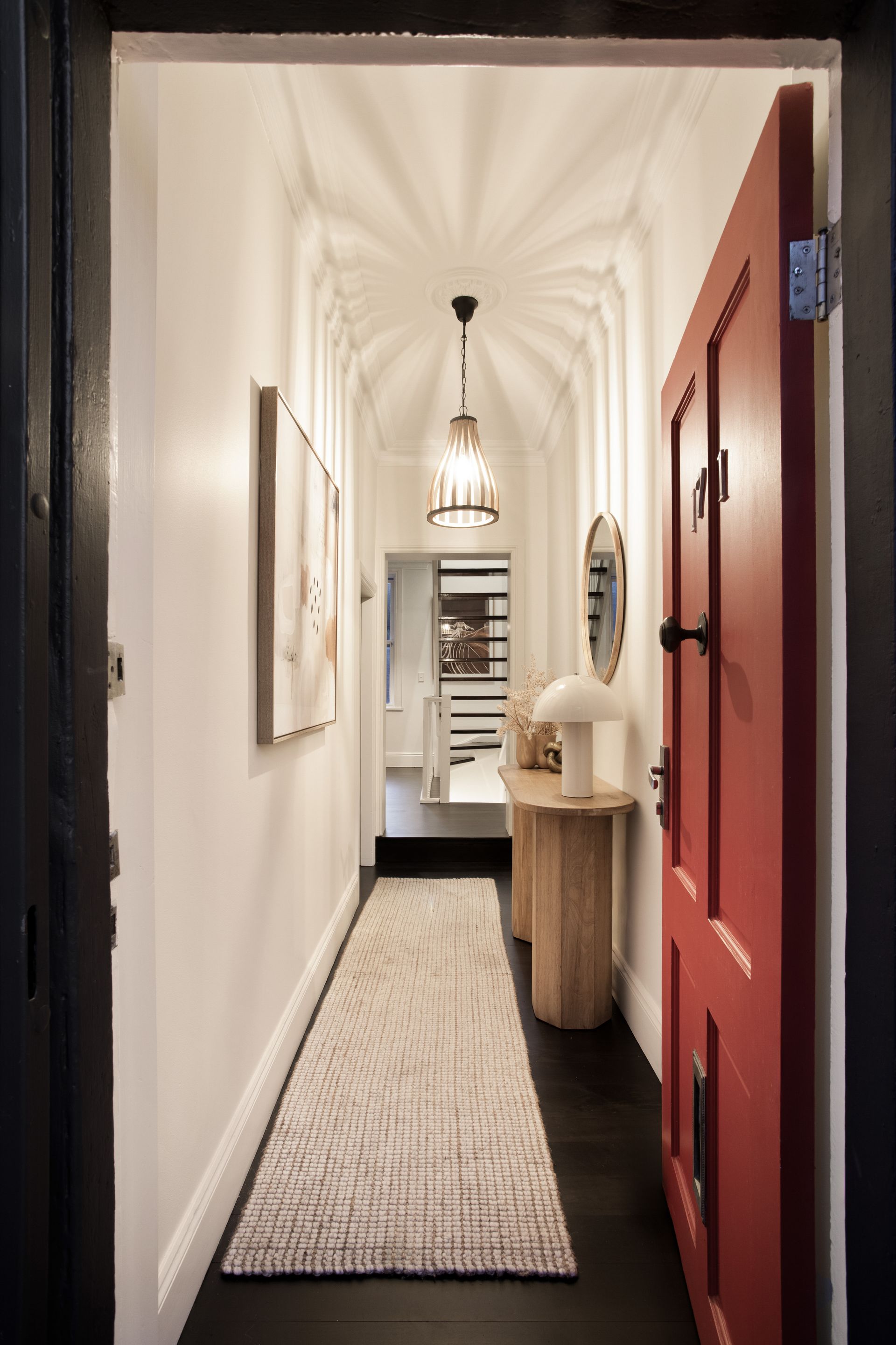 Narrow hallway with a red door, white arched ceiling, woven runner, and small table at the far end.