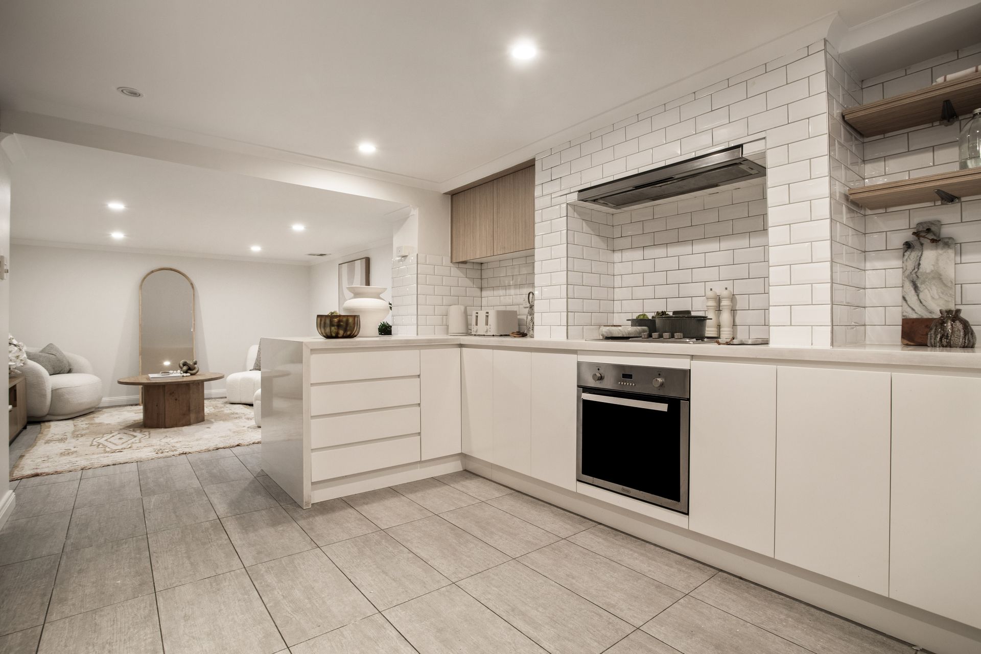 Modern white kitchen with island, built-in oven, subway tile backsplash, and open shelving in a bright living space