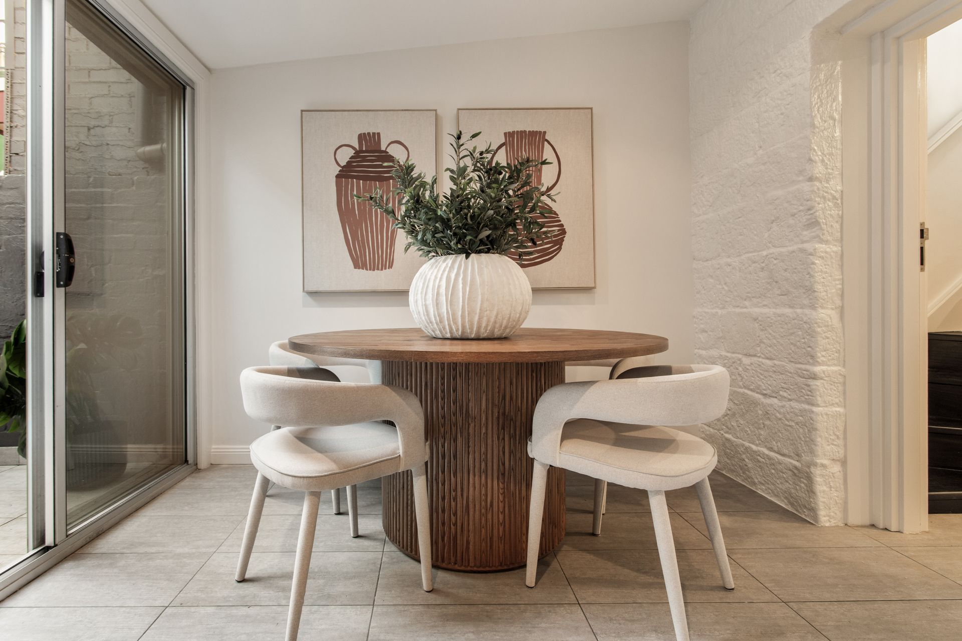 Modern dining nook with a round wooden table, four white chairs, and large pottery art on the wall