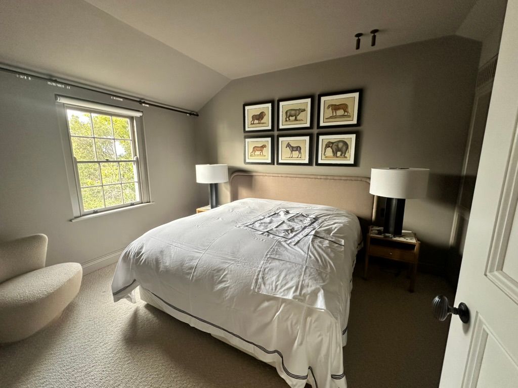 Bright bedroom with made bed, gray walls, framed art, and bedside lamps