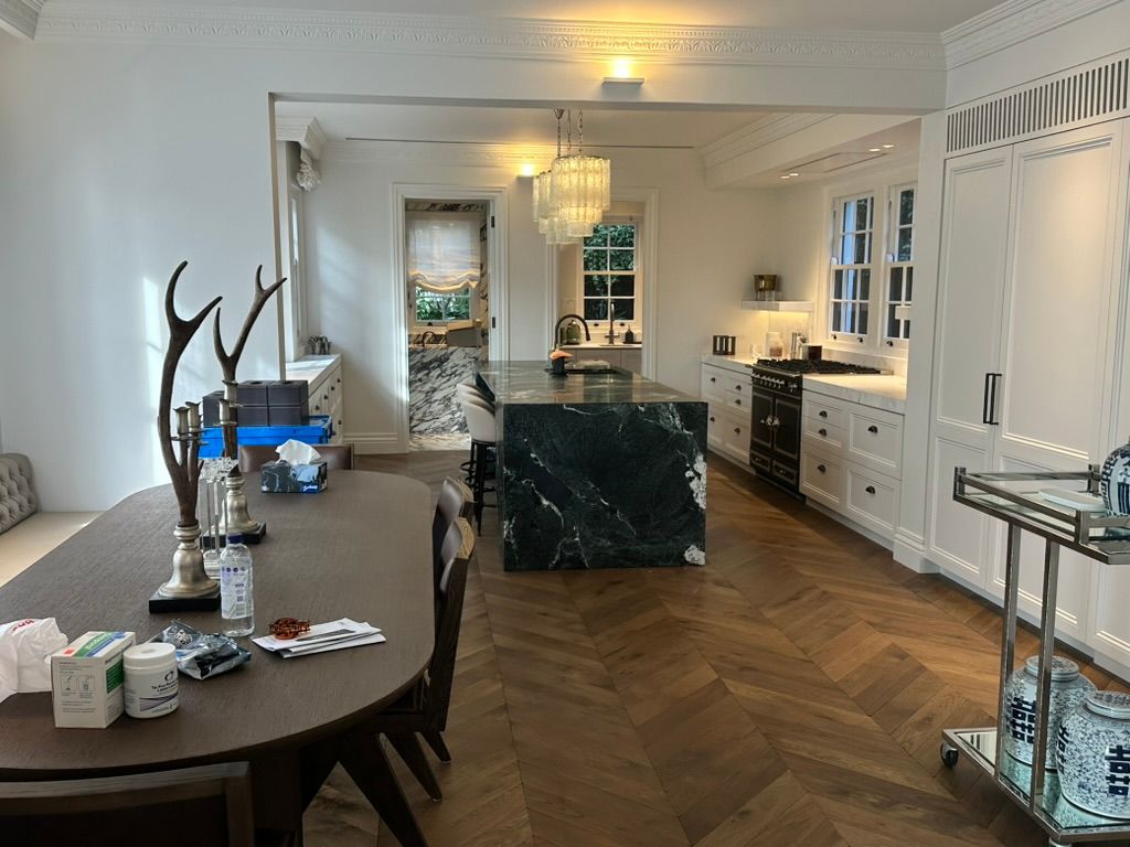 Elegant white dining and living room with wooden herringbone floor, chandelier, and a large marble island.