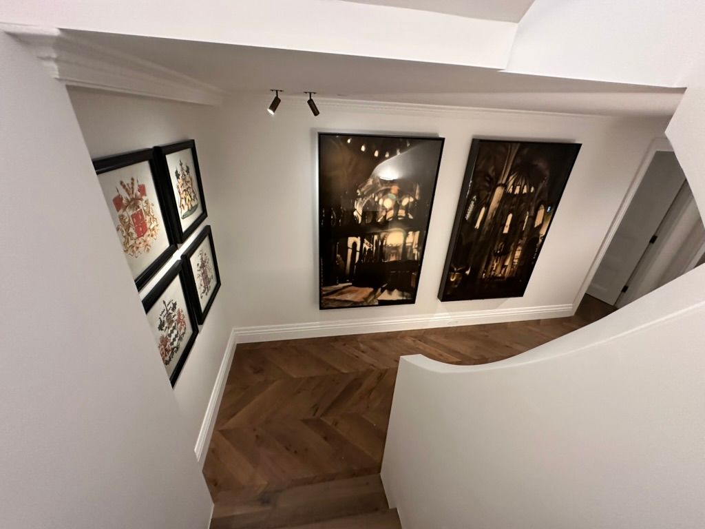Art gallery hallway with framed paintings and large wall-mounted photographs, white walls, and herringbone wood floor