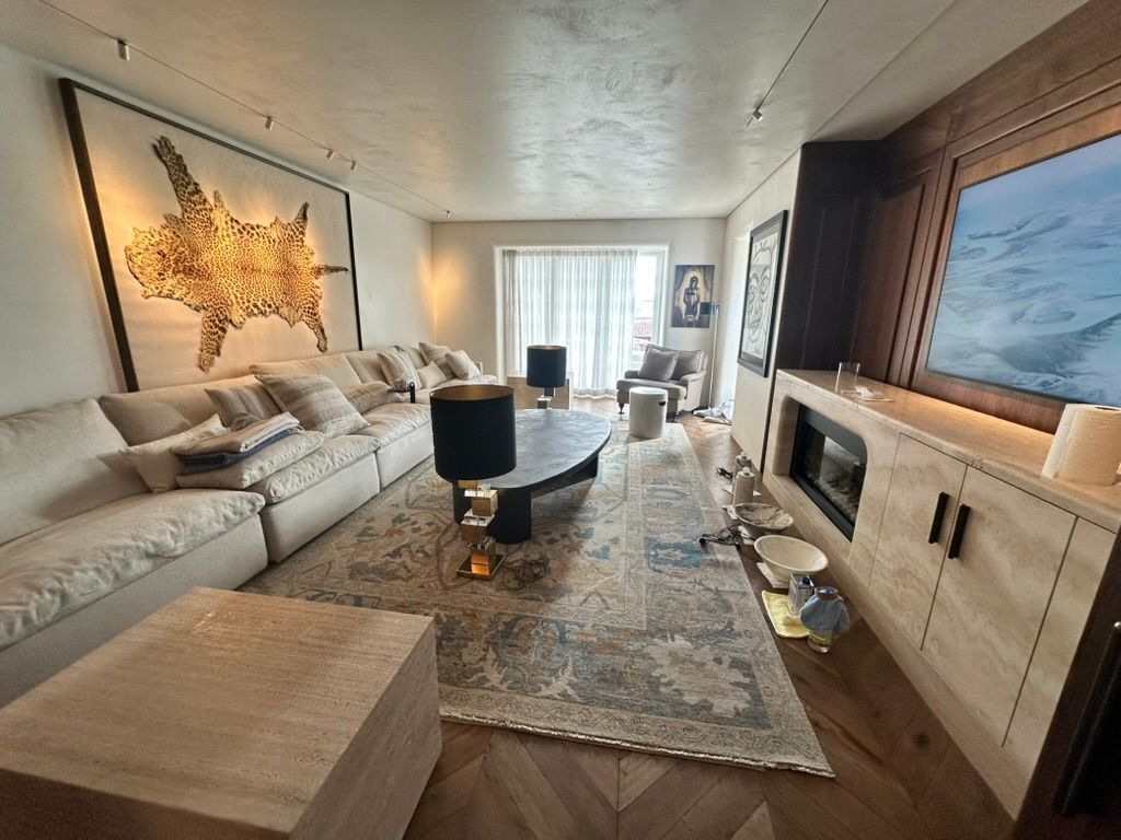 Bright modern living room with cream sectional, black coffee table, large rug, and TV on a wood-paneled wall.