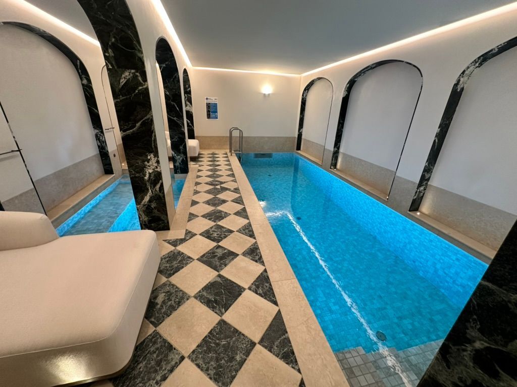 Indoor pool with bright blue water, black-and-white tiled floor, and arched seating alcoves