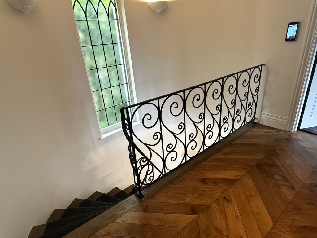 Stairwell with black iron railing, wooden herringbone floor, and frosted window on a white wall