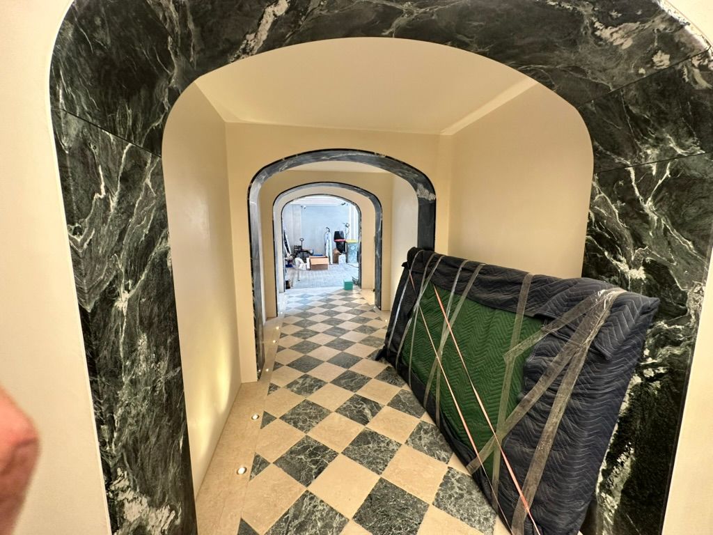 Narrow hallway with diamond tile floor, arched doorways, and stacked mattresses along the right wall.