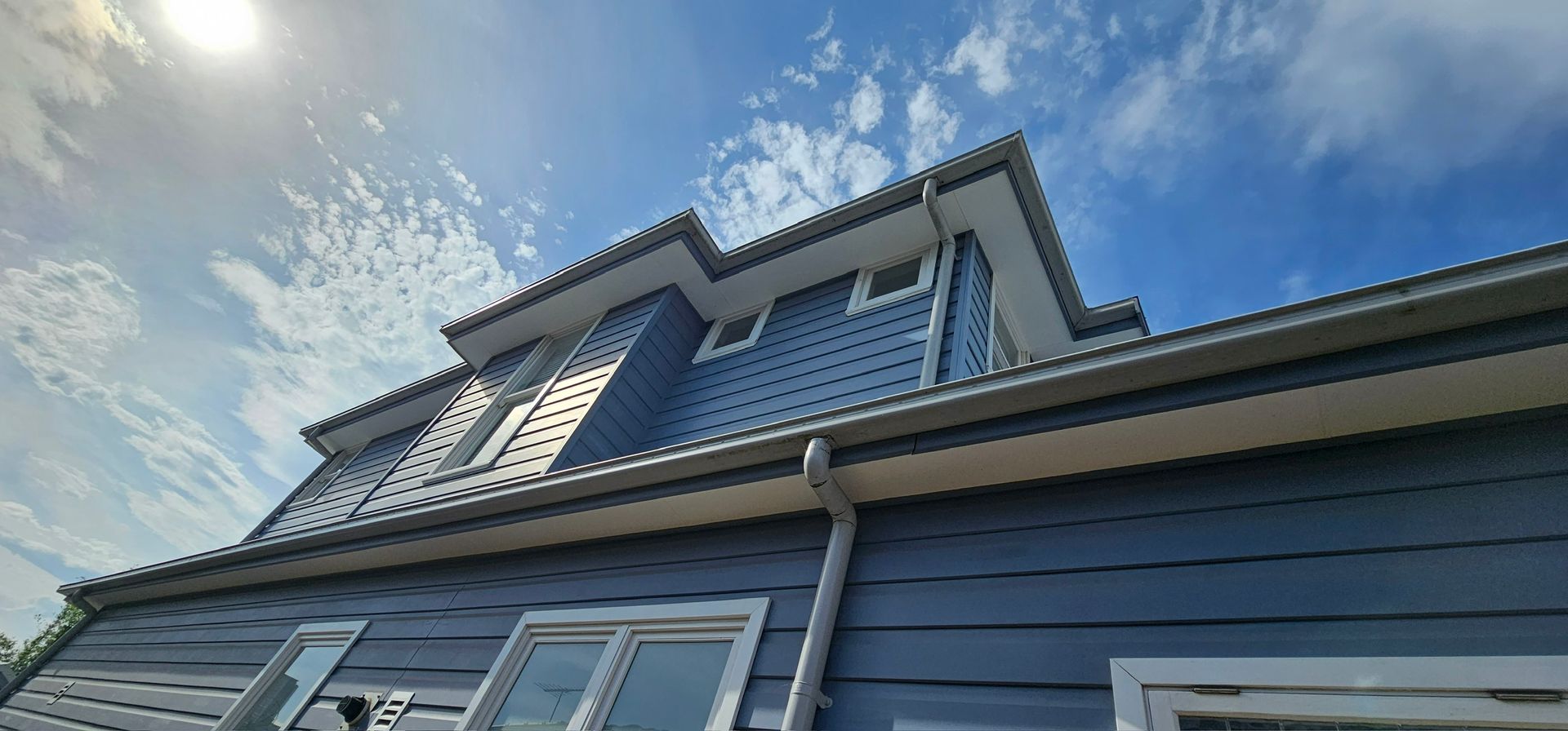 Blue house exterior with steep dormer windows under a partly cloudy sky