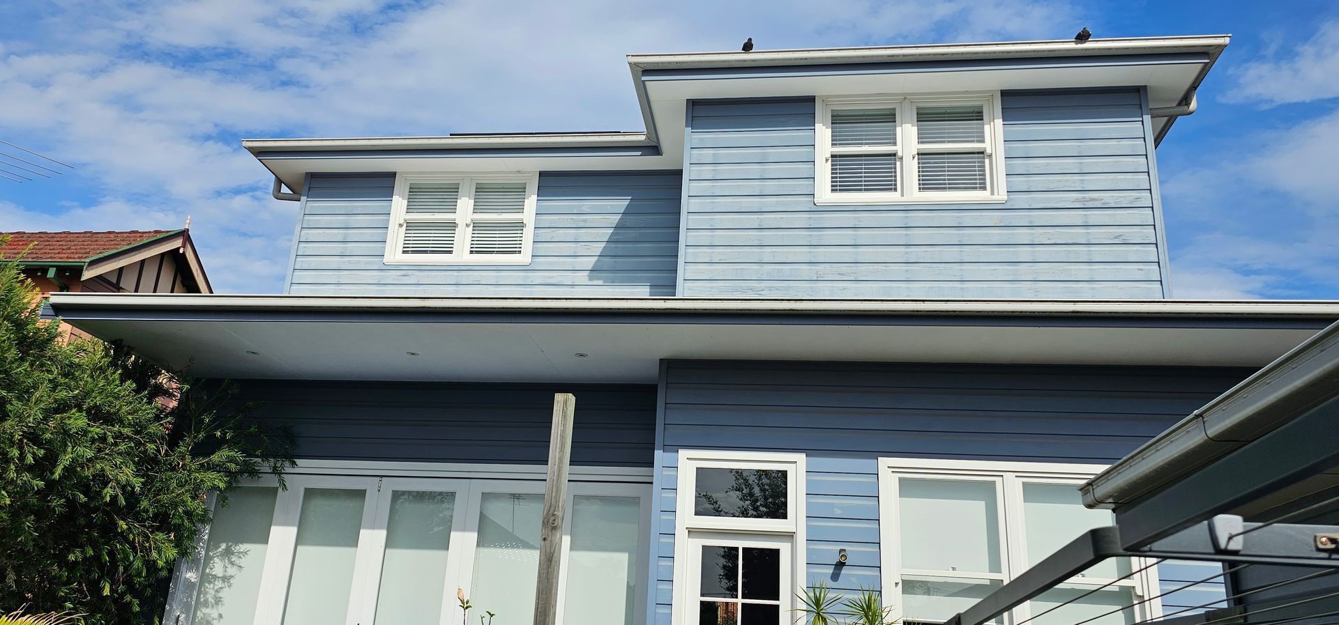 Blue two-story house exterior with white trim and a covered porch under a clear sky