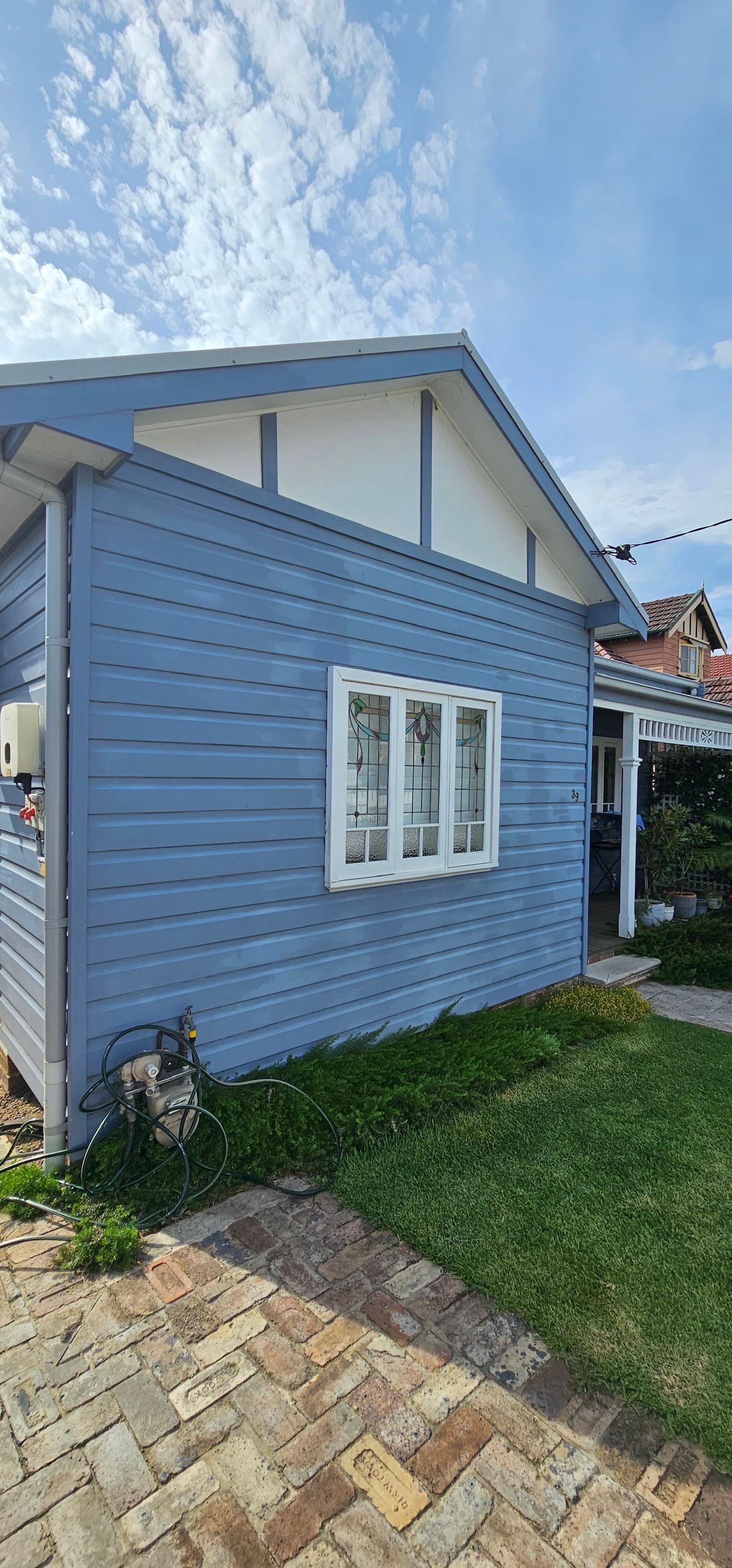 Blue house exterior with white trim, small windows, grassy yard, and paved walkway under a cloudy sky