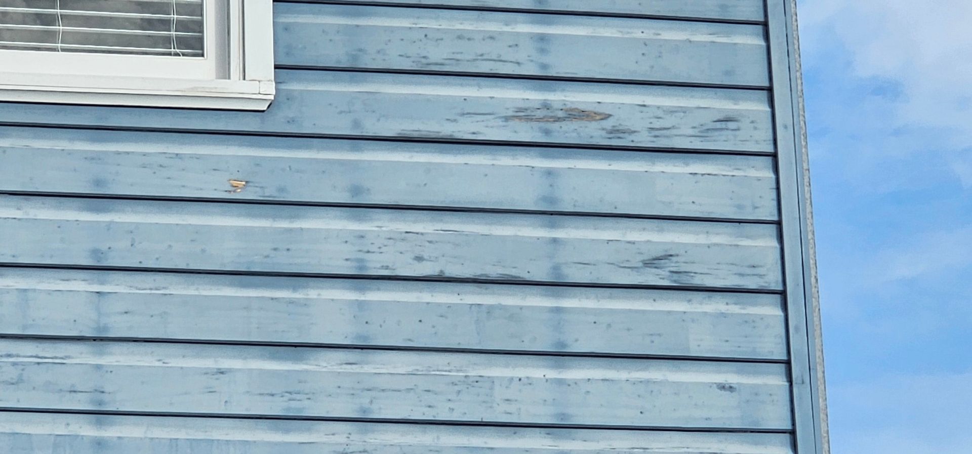 Light blue wooden house siding with a white window against a blue sky