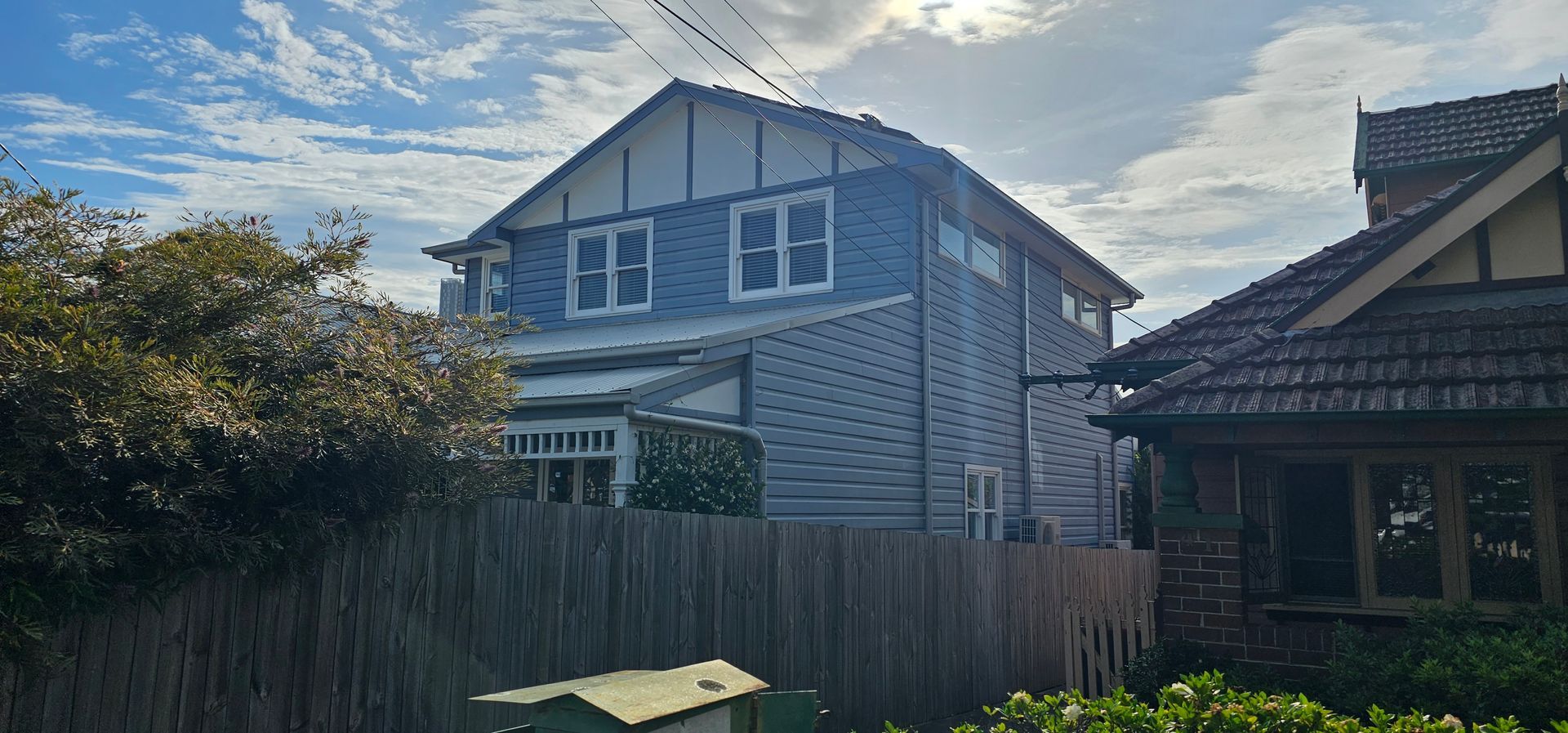Two-story gray house with white trim behind a wooden fence under a cloudy sky