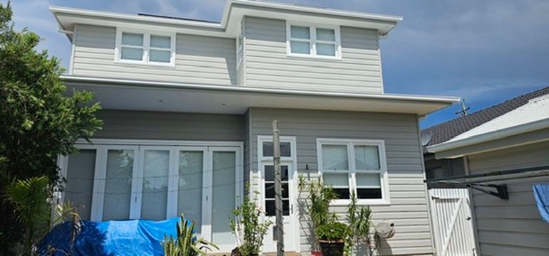 Two-story gray house with white trim and a blue tarp in the front yard