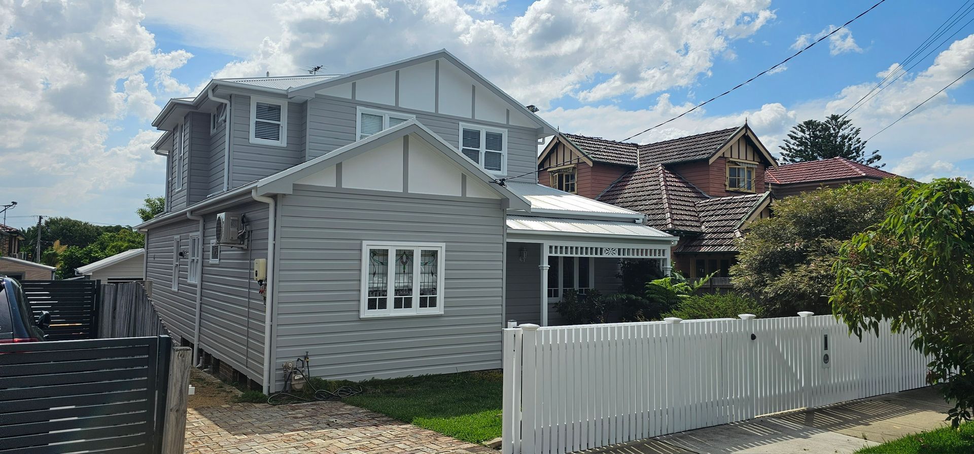 Two-story gray house with white trim and fenced front yard on a sunny street