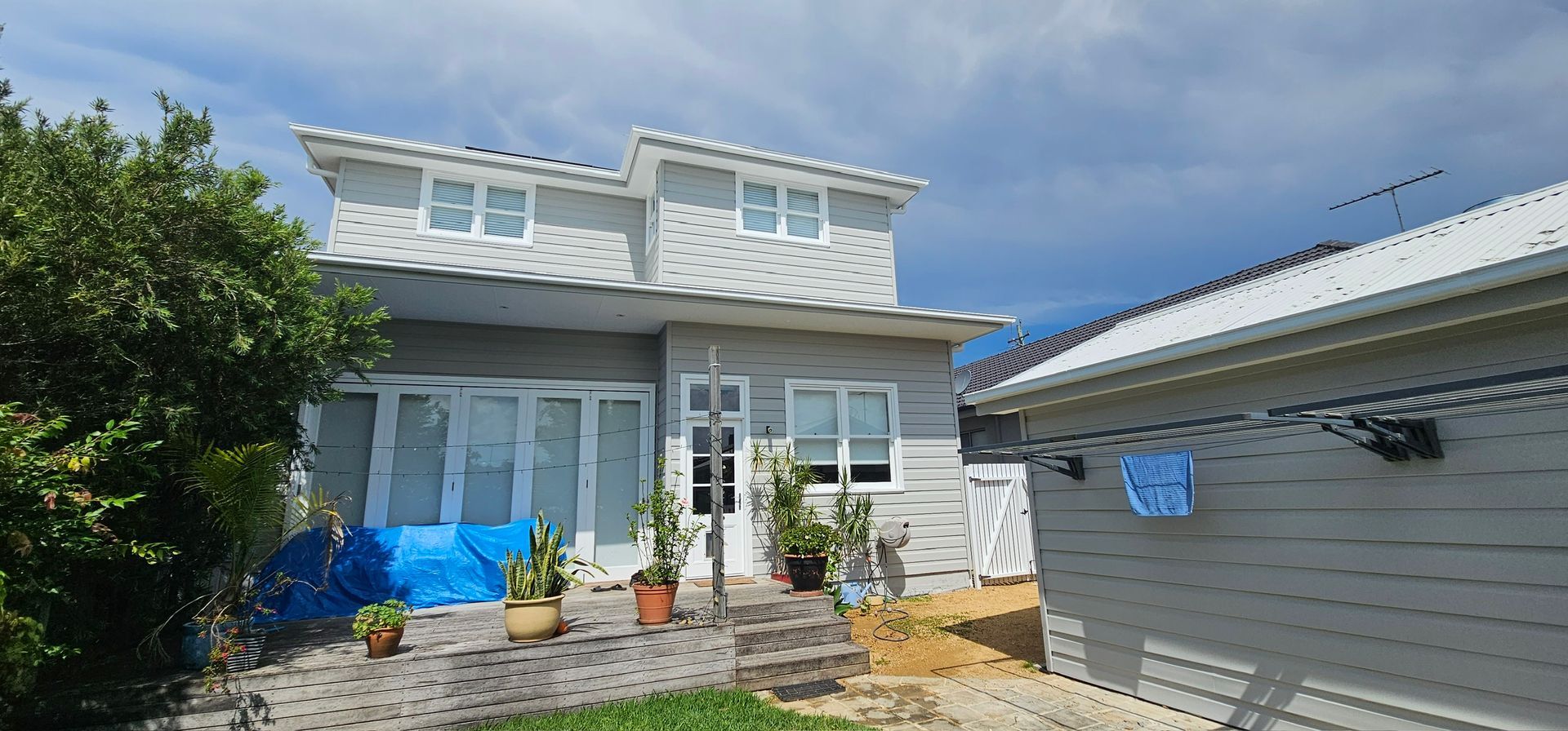 White two-story house with blue awnings, front steps, potted plants, and a garage on the right
