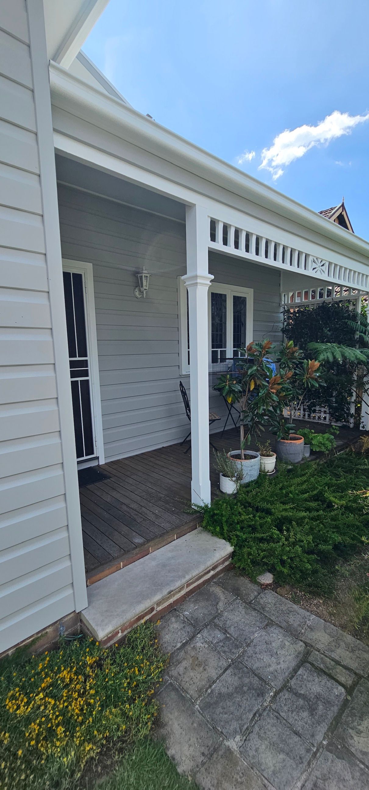 Front porch of a white house with potted plants, columns, and a stone walkway.