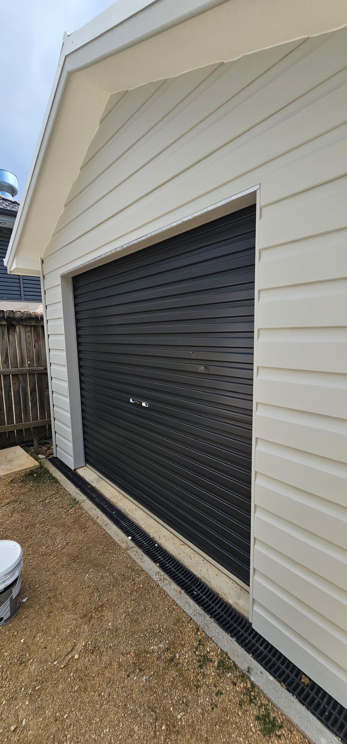 Black roller garage door on a white-sided house exterior, viewed at an angle.