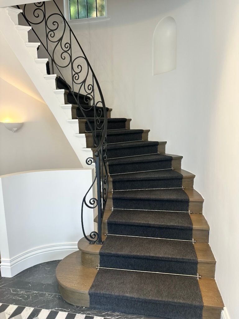 Curved black staircase with patterned runner and wrought-iron railing in a white interior hallway