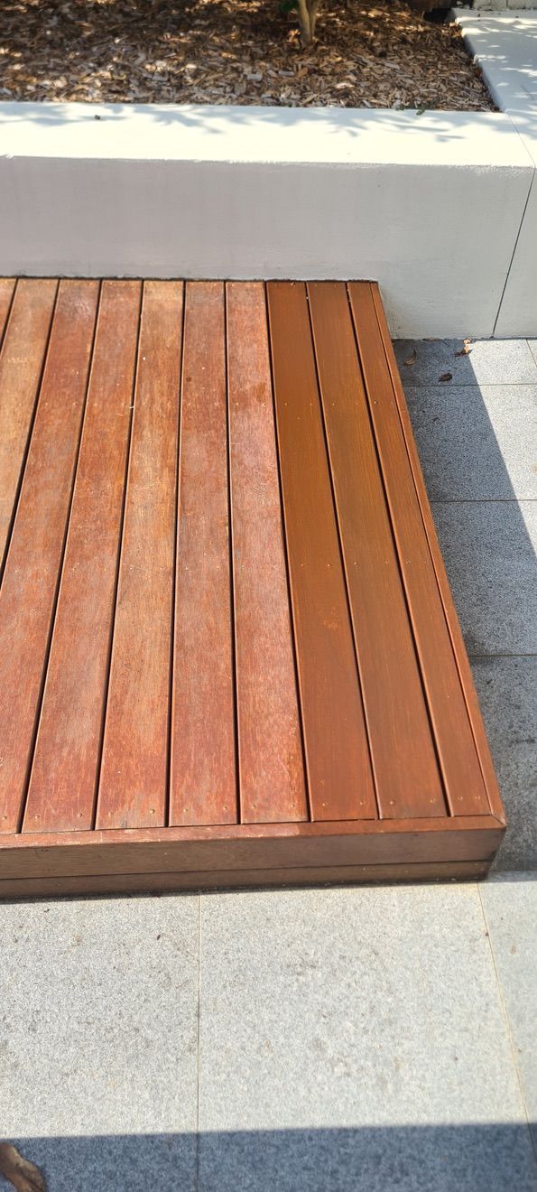 Wooden slatted bench beside a white concrete wall on a paved sidewalk.