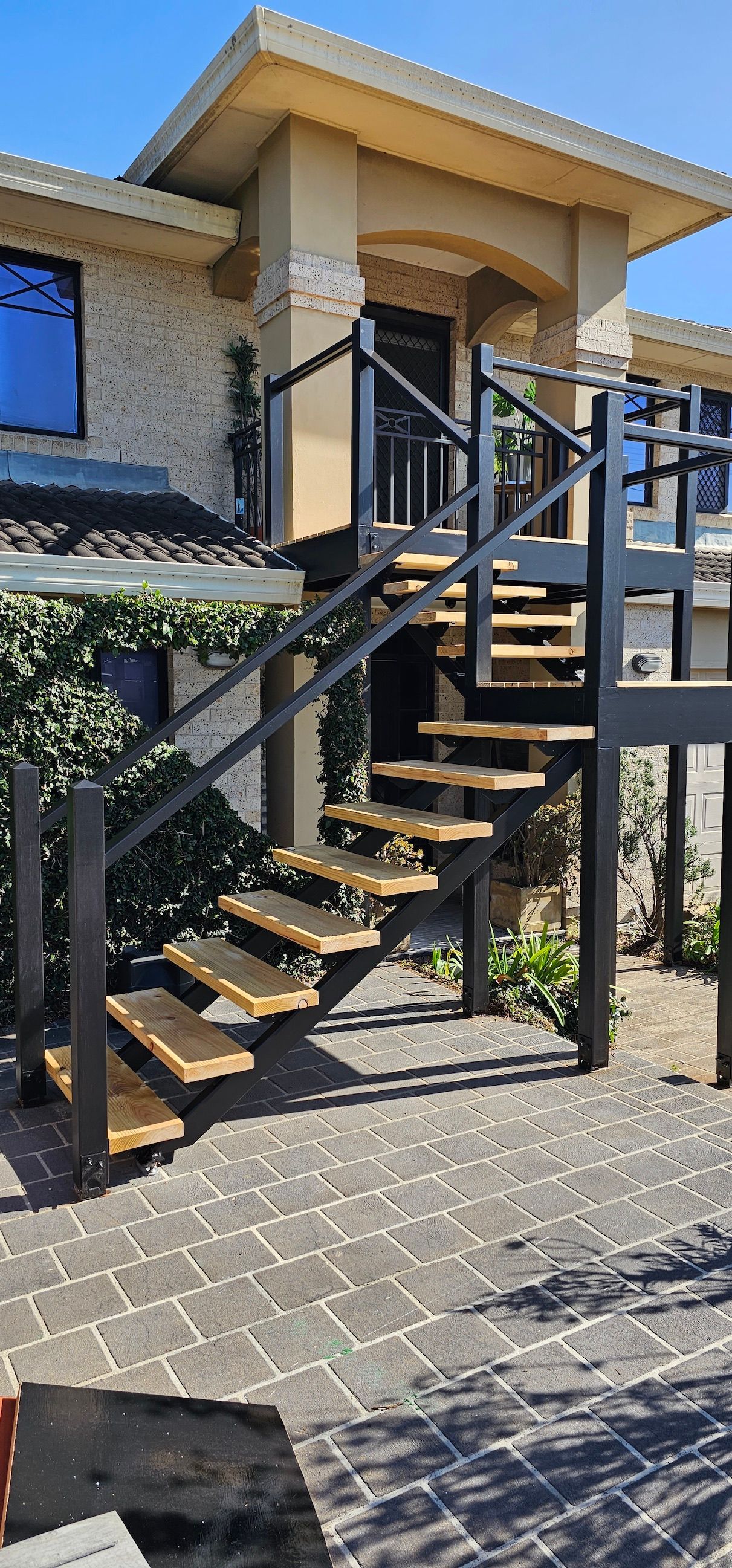 Exterior staircase with black metal railings and wooden steps beside a tan building