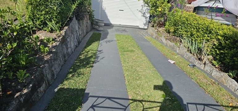Steep driveway with black-and-gray paving, narrow grass center strip, stone walls, and greenery on both sides Steep driveway with black-and-gray paving, narrow grass center strip, stone walls, and greenery on both sides