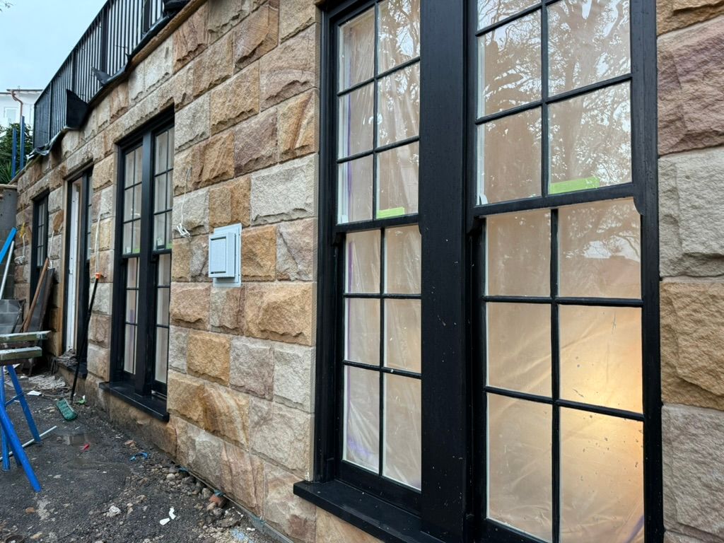 Stone building exterior with tall black-framed windows and a narrow gravel alley