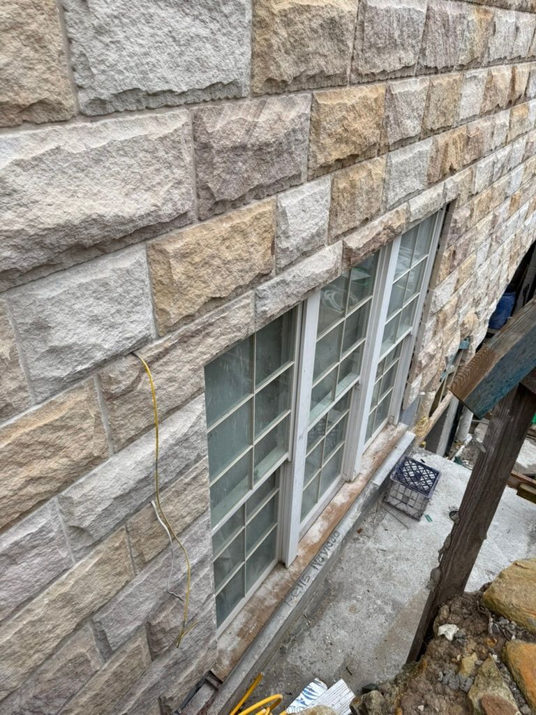 Stone building wall with tall windows overlooking a narrow exterior basement walkway