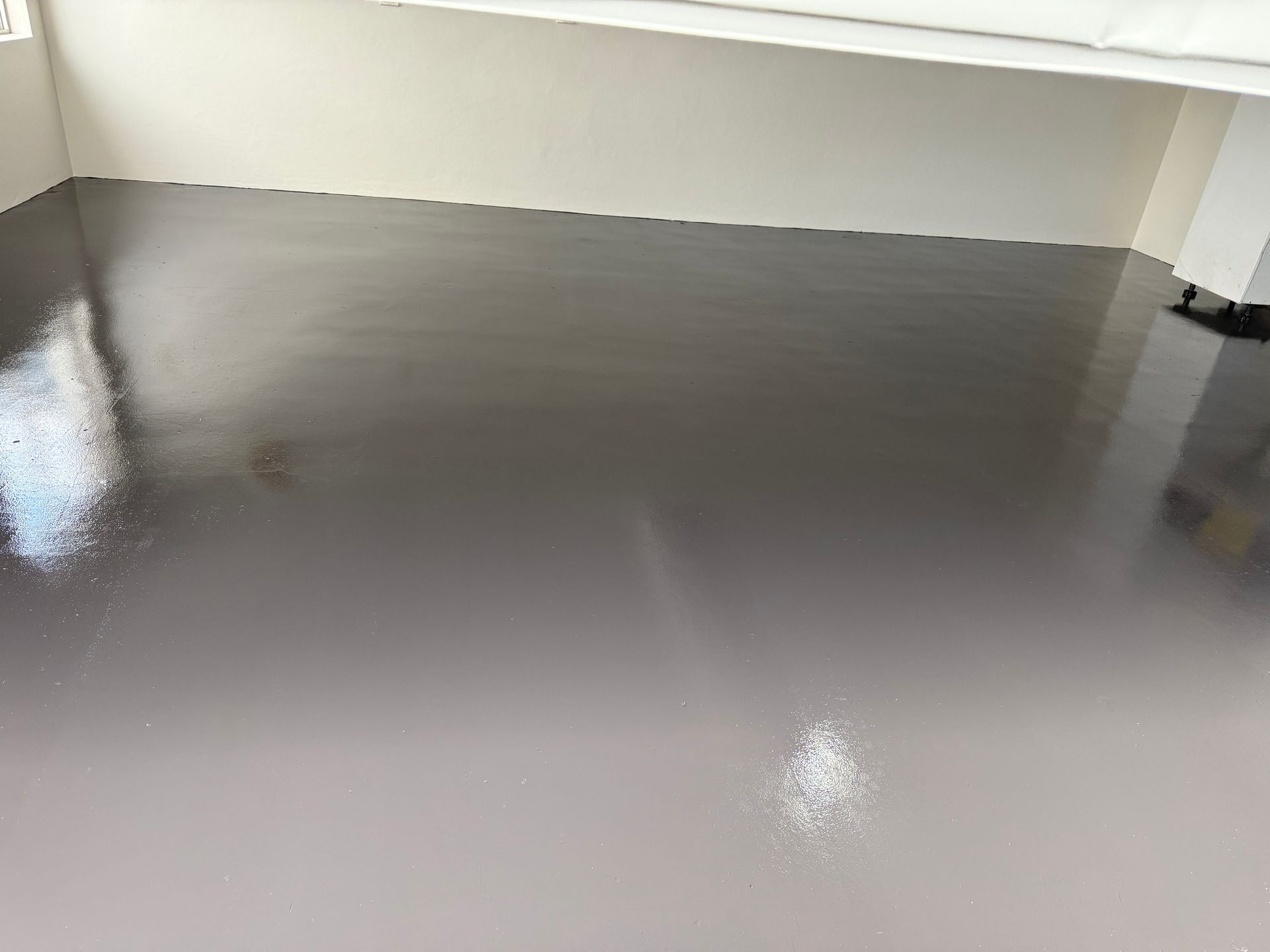 Freshly coated gray floor in an empty room, with a glossy sheen and white walls. Freshly coated gray floor in an empty room, with a glossy sheen and white walls.