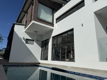 Modern white house with large windows beside a swimming pool under a clear blue sky