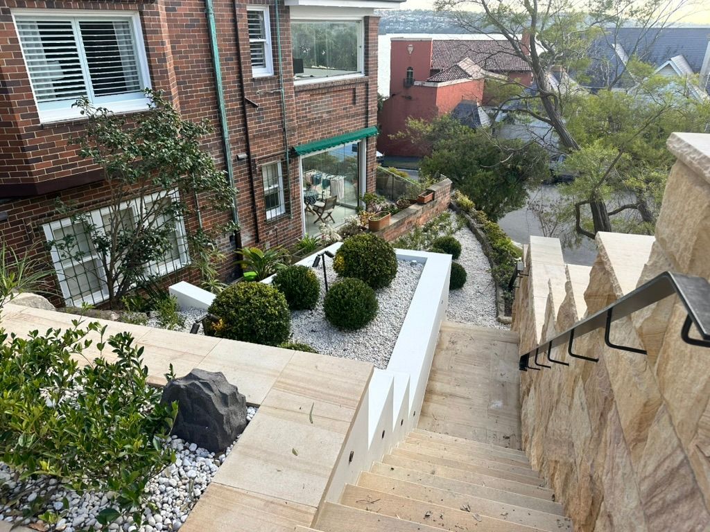Steep outdoor stairs beside brick houses, with trimmed shrubs and a garden path below.