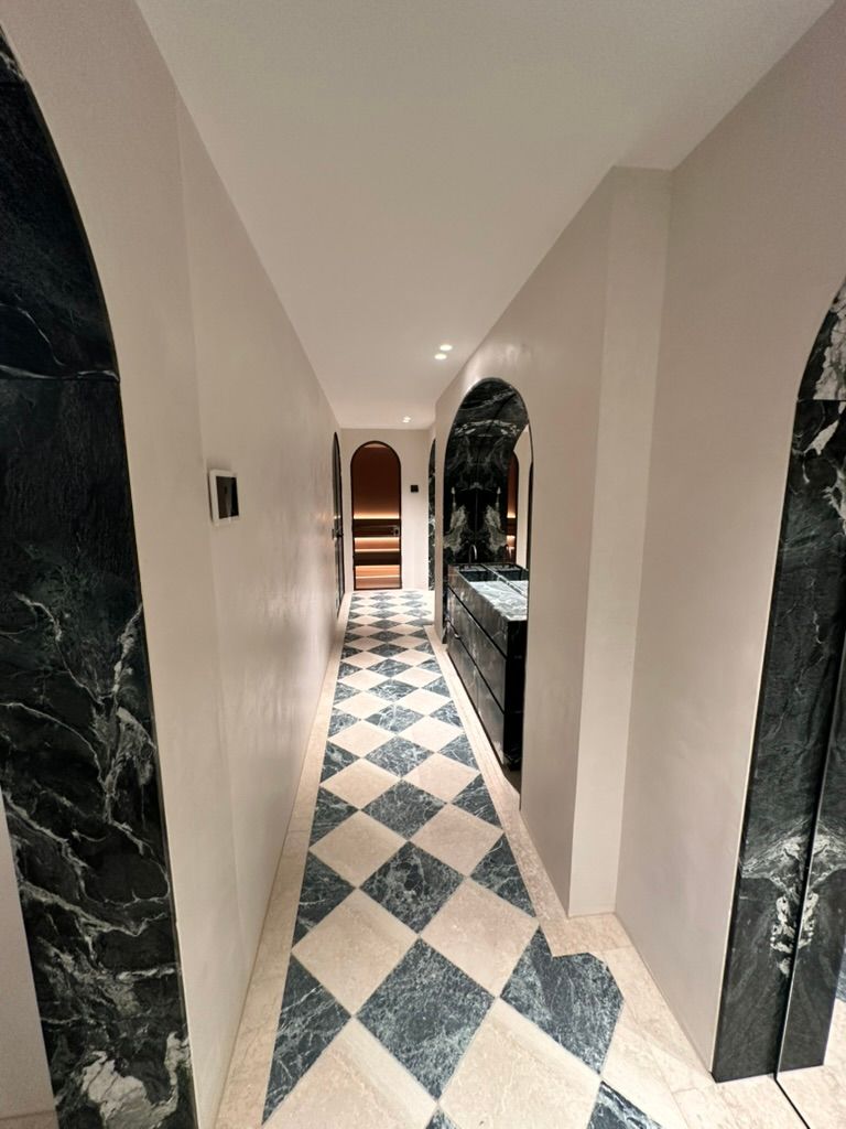 Narrow hallway with black-and-white diamond tile floor, arched openings, and recessed ceiling lights
