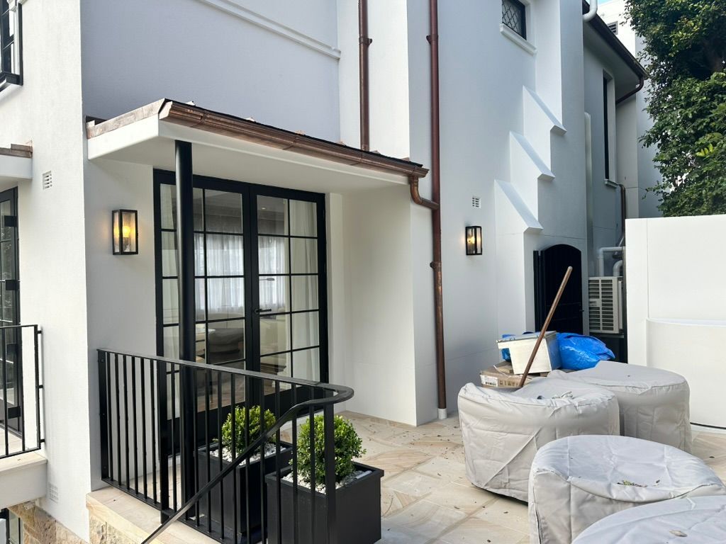Small patio beside a white townhouse with black railing, wall lanterns, and covered furniture under renovation. Small patio beside a white townhouse with black railing, wall lanterns, and covered furniture under renovation.