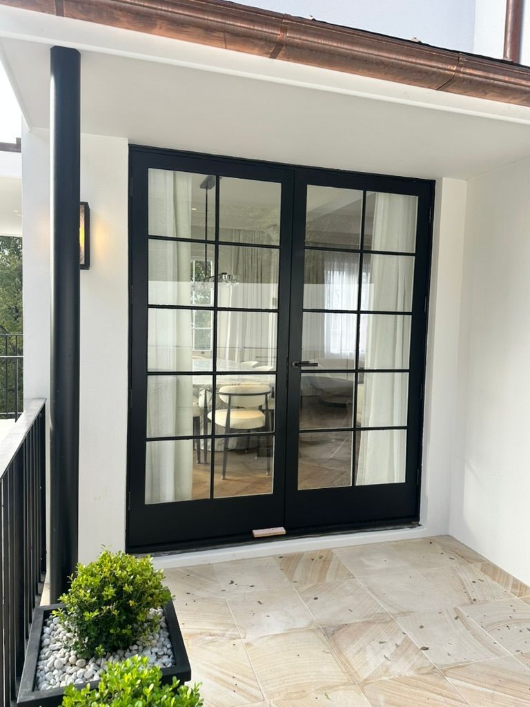 Black-framed French doors opening to a bright covered porch with beige tile floor and potted greenery