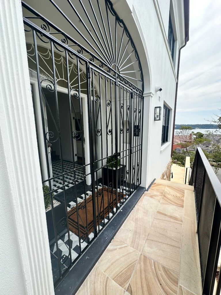 Narrow outdoor walkway beside a white building with black iron gates, potted plant, and sea view.