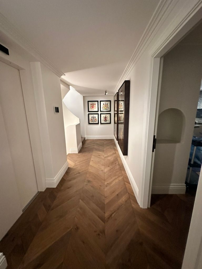 Narrow hallway with herringbone wood floor, white walls, framed art, and an open doorway to the right