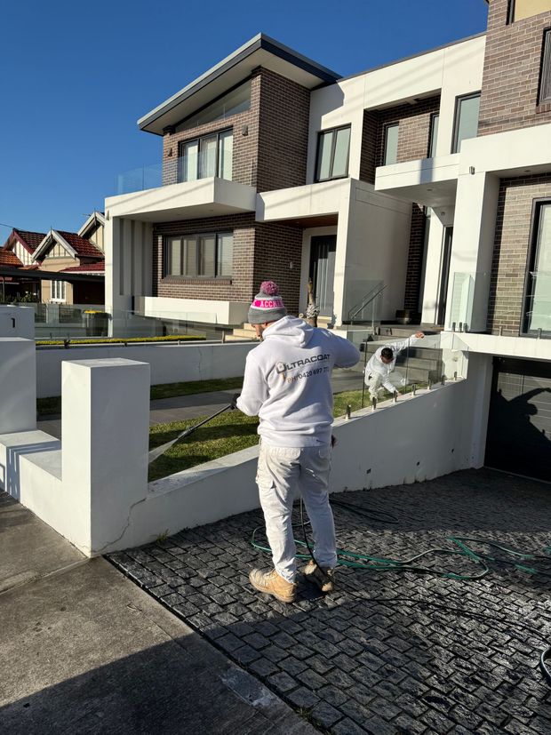 Worker in white uniform and pink hat walking toward modern townhouse in a sunny residential neighborhood