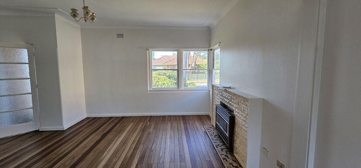 Empty living room with striped wood floor, white walls, fireplace, and a window letting in daylight Empty living room with striped wood floor, white walls, fireplace, and a window letting in daylight