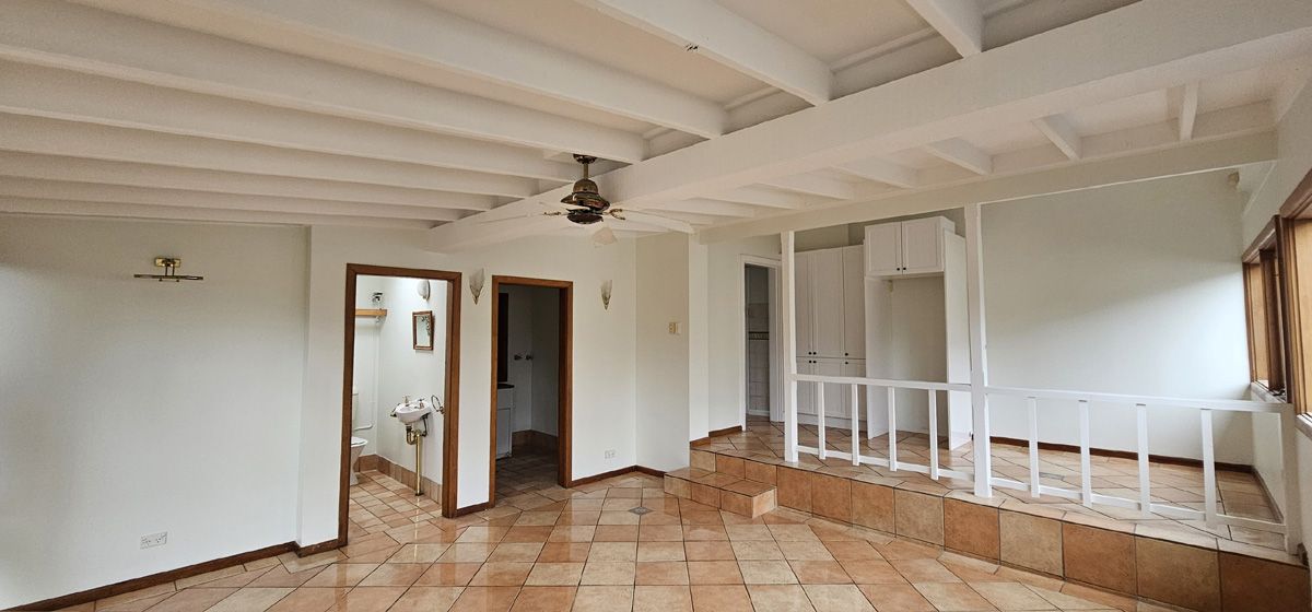 Empty white room with terracotta tile floor, exposed beams, and a small doorway on the left Empty white room with terracotta tile floor, exposed beams, and a small doorway on the left