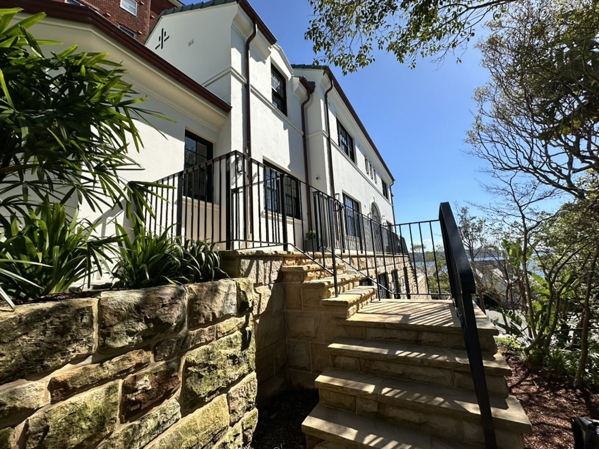Stone steps beside a white townhouse and stone wall under a blue sky