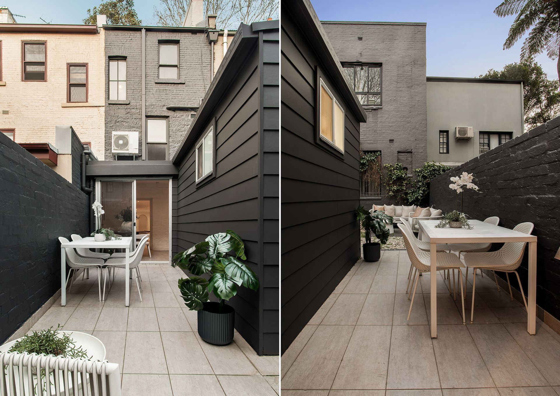 Narrow outdoor patio with two white dining tables, potted plant, and dark gray siding between row houses.
