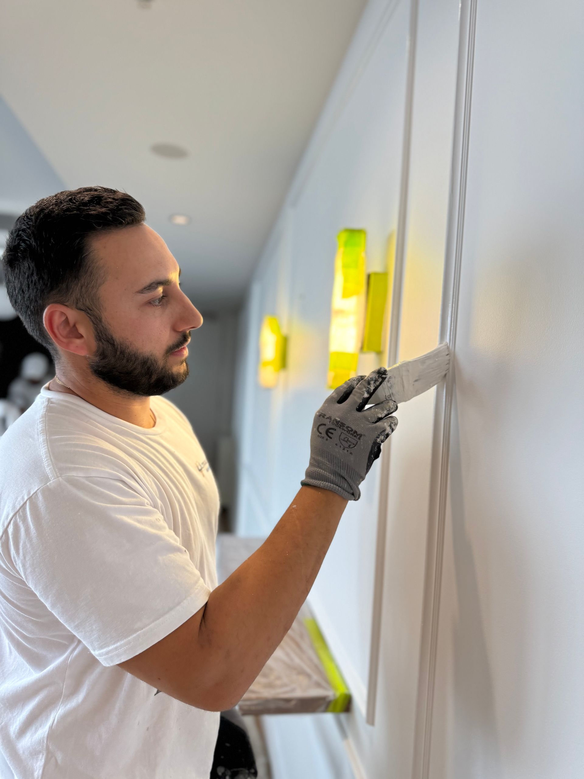 Worker in gloves painting a white wall with a roller in a bright hallway Worker in gloves painting a white wall with a roller in a bright hallway
